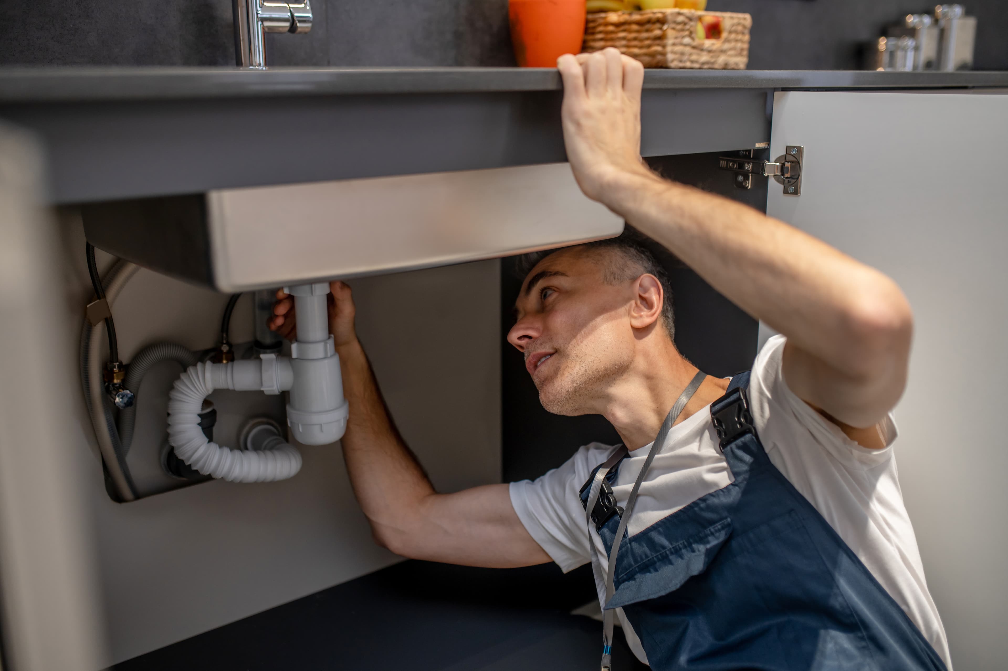 Licensed plumber carefully repairing pipes under a kitchen sink